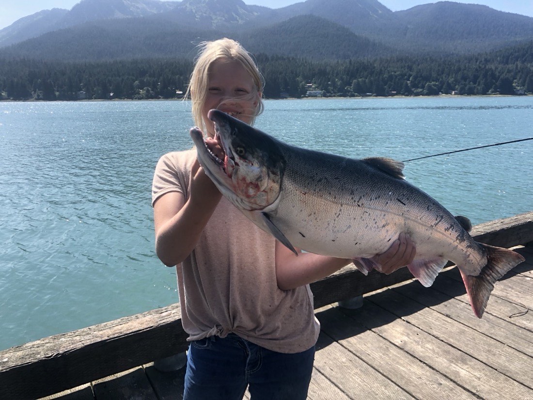 Courtney Skinner holding a silver salmon with mountains behind, Juneau Alaska